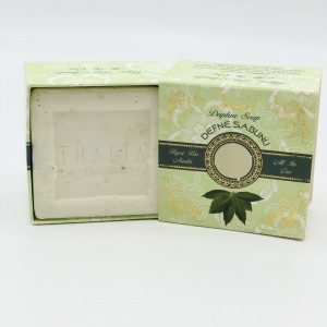 Open light green box with dark green line and picture of Bay Leaf showing a square, white bar of Organic Bay Leaf Soap.