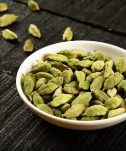 White bowl filled with Cardamom Pods and some spread on the table around the bowl.