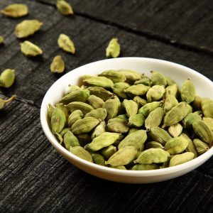 White bowl filled with Cardamom Pods and some spread on the table around the bowl.