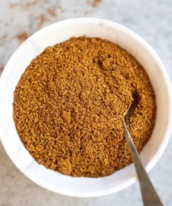 White bowl filled with Ground Cumin Seed and inside a silver coloured spoon