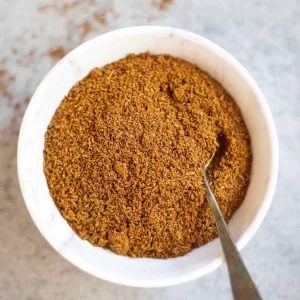 White bowl filled with Ground Cumin Seed and inside a silver coloured spoon