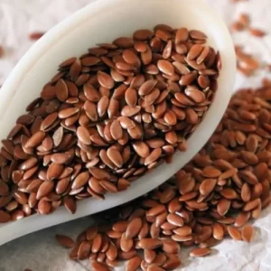 White spoon filled with Whole Flaxseed, overflowing and some Whole Flaxseed spilled on the table