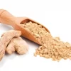 A wooden spice spoon overflowing with Ground Ginger. Flanked by two Dried Ginger Roots