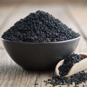 Bowl with a pile of Black Cumin Seeds, with a wooden spice spoon on the side filled with Black Cumin Seeds