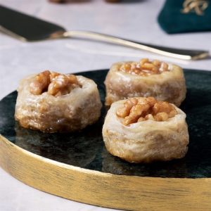 Marble flat plate with golden rim showing three pieces of walnut Burma baklava.