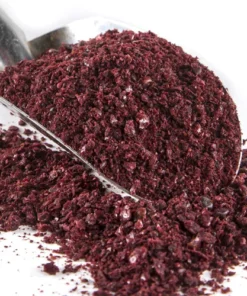 Silver coloured scoop with a pile of purple sumac spice on a bed of more sumac spice